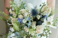 a textural wedding bouquet with blue thistles, white blooms, various greenery looks natural and a bit wild
