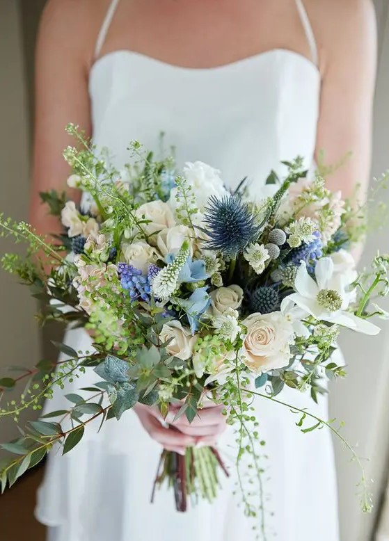 a textural wedding bouquet with blue thistles, white blooms, various greenery looks natural and a bit wild