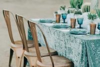 a turquoise velvet tablecloth with blue plates and amber glasses for a desert wedding table setting