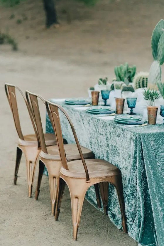 a turquoise velvet tablecloth with blue plates and amber glasses for a desert wedding table setting
