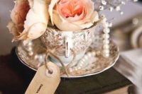 a vintage wedding centerpiece of a book stack, a tag, a vintage cup with blooms and soem pearl strands