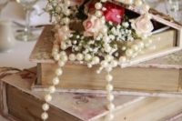 a vintage wedding centerpiece of a stack of books, blooms and stands of pearls looks super elegant and very chic