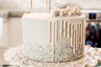 a white wedding cake with beads, glitter and pieces of white chocolate on top plus sparklers is very modern and lovely