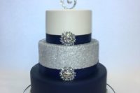 an elegant white, silver and navy wedding cake with glitter, embellishments and an embellished monogram on top
