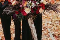 an oversized colorful wedding bouquet with red, pink, purple, peachy, orange blooms, dark foliage and greenery to stand out with a black wedding dress