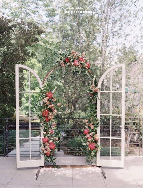 arched French doors with greenery and coral blooms are a beautiful and chic wedding backdrop