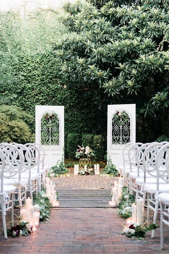 beautiful and refined white doors with metal detailing, neutral blooms and greenery, greenery and pillar candles on the ground