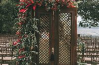 dark stained double doors decorated with greenery and red blooms plus tropical foliage around for a hot climate wedding
