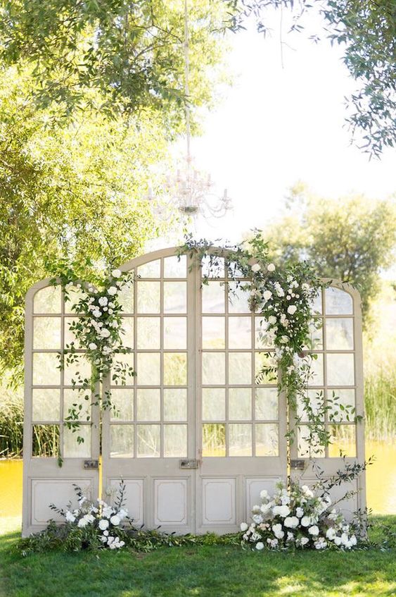 large and beautiful French doors decorated with greenery and white blooms are a sophisticated and chic wedding backdrop