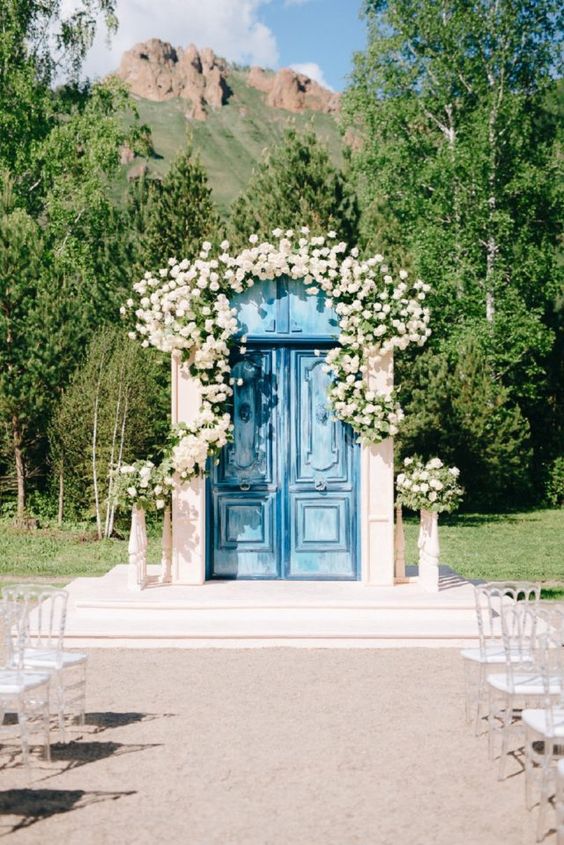 refined blue shabby chic double doors decorated with neutral blooms and greenery are a lovely wedding backdrop for a chic ceremony