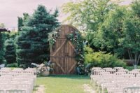 rustic arched barn doors decorated with greenery and pastel blooms, with matching blooms in a planter for a rustic wedding