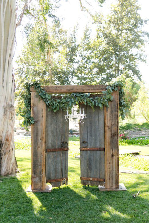 rustic vintage double doors decorated with a chandelier and some greenery are a beautiful and cozy wedding backdrop