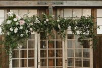 shabby chic French doors topped with greenery, blush and white blooms and with pillar candles in glasses are a beautiful wedding backdrop