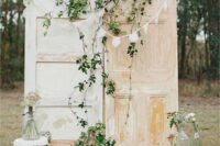 shabby chic doors with greenery, a bunting, a stack of vintage suitcases, greenery and a stool are a beautiful vintage backdrop for a wedding