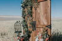 stained arched doors with greenery, dried blooms, orange and white fresh ones, greenery and a cage for a rustic wedding