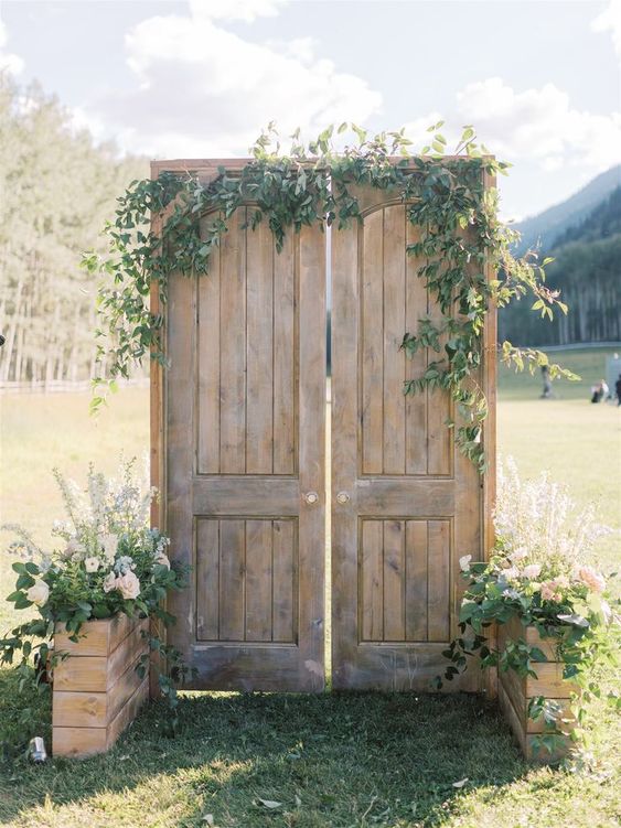 stained double doors decorated with greenery, with planters with greenery and blush blooms are a cool rustic wedding idea