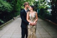 the groom wearing a black suit and a tie and the bride rocking a gold wedding dress with a train