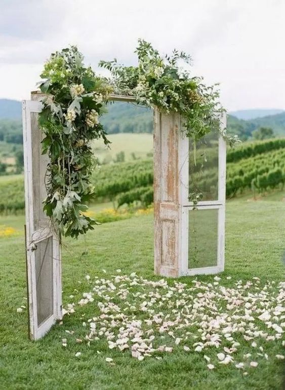 vintage double doors decorated with greenery and white blooms, with white petals on the grass are a lovely wedding backdrop