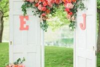 white double doors decorated with monograms and coral and blush blooms plus greenery on top plus matching arrangements on both sides