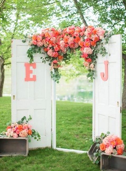 white double doors decorated with monograms and coral and blush blooms plus greenery on top plus matching arrangements on both sides
