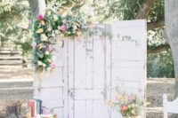 white shabby chic doors decorated with greenery and bright pink and yellow blooms, stacked vintage suitcases and books for a vintage wedding
