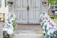 white shabby chic doors with greenery, purple blooms, purple monograms and bold blooms lining up the aisle