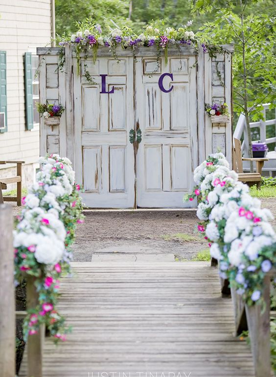white shabby chic doors with greenery, purple blooms, purple monograms and bold blooms lining up the aisle