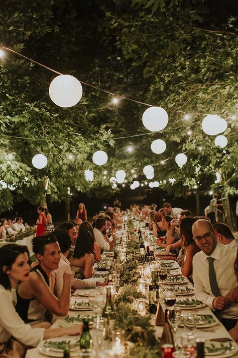 a beautiful and welcoming outdoor wedding reception with greenery and candles on the tables, paper lanterns and string lights over them for more coziness