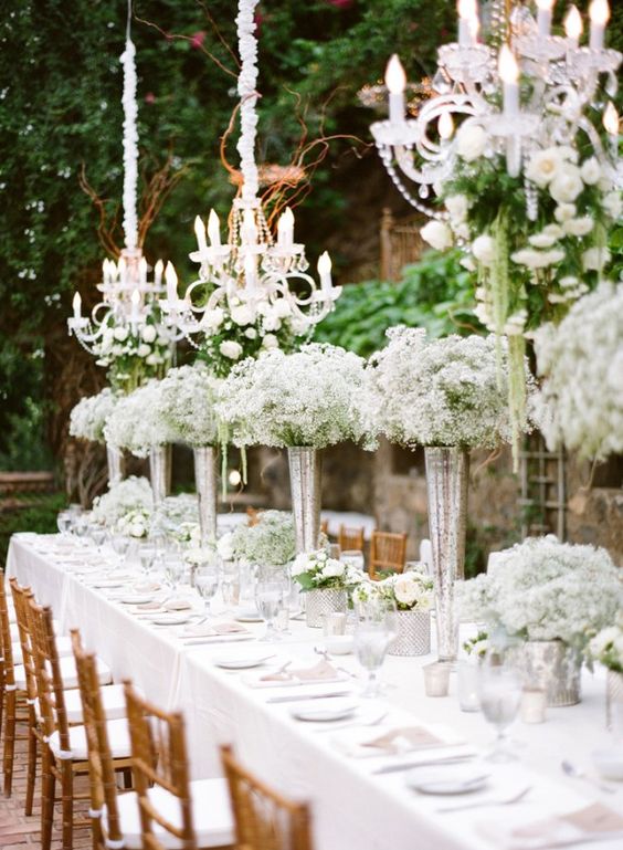 a beautiful outdoor wedding reception with baby's breath arrangements and crystal chandeliers over the table is amazing
