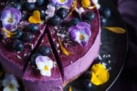 a blueberry cheesecake with fresh flowers and berries on top is a delicious dessert idea for a wedding