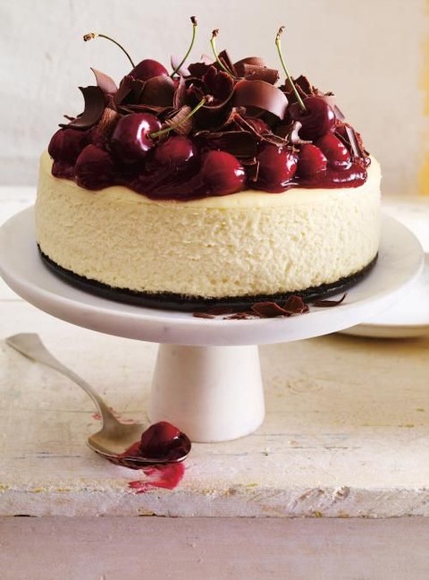a cheesecake topped with milk chocolate shaves and fresh cherries will make everyone happy