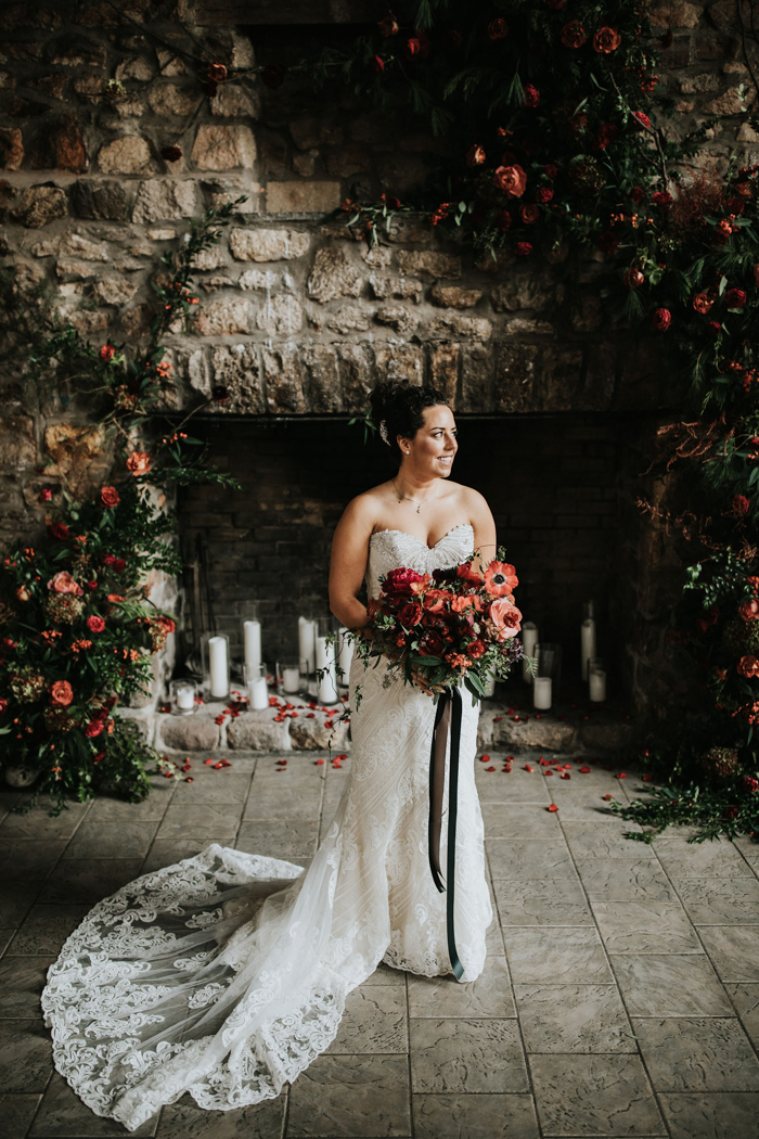 a chic strapless lace sheath wedding dress with a train and carrying a red and pink wedding bouquet