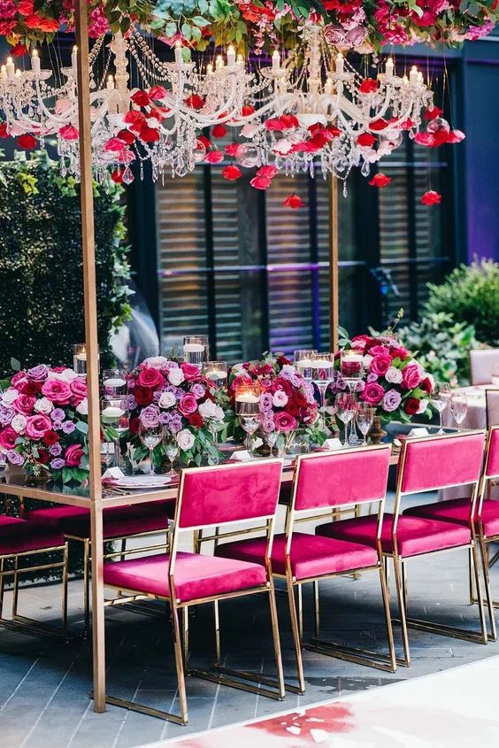 a colorful wedding reception with super bold florals and chairs, crystal chandeliers covered with pink and red blooms