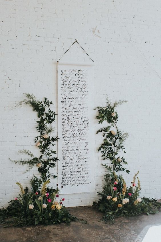 a cool wedding backdrop with a long quote, greenery and bright blooms is a very creative and cool decor idea for a modern wedding