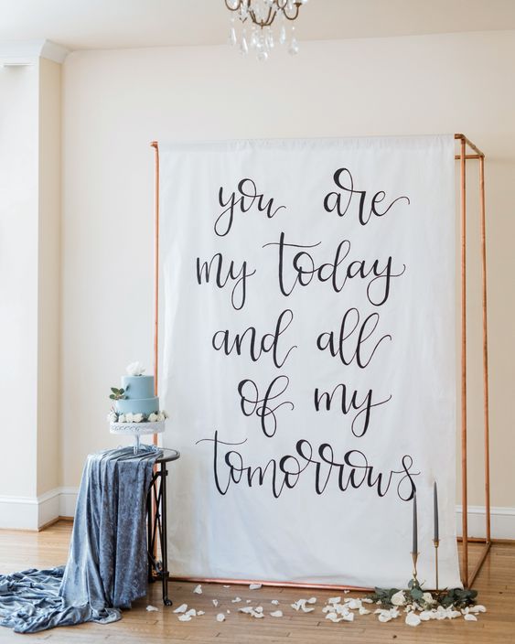 a copper frame with a large quote, candles and petals around is a good idea of a modern and romantic wedding backdrop