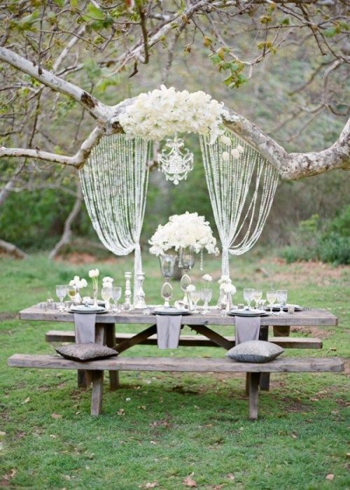 a creative woodland wedding reception under a tree, with weathered wood branches and a table, a branch decorated with lush florals, crystals and a chandelier