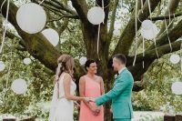 a delicate rustic wedding ceremony space with tree stumps and candles, a living tree with white paper lanterns is wow