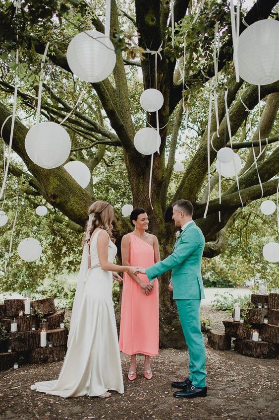 a delicate rustic wedding ceremony space with tree stumps and candles, a living tree with white paper lanterns is wow