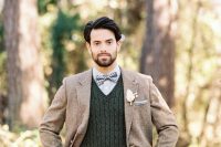 a fall groom’s outfit with a grey shirt, a plaid bow, hunter green cable knit jumper, a brown tweed blazer and navy pants