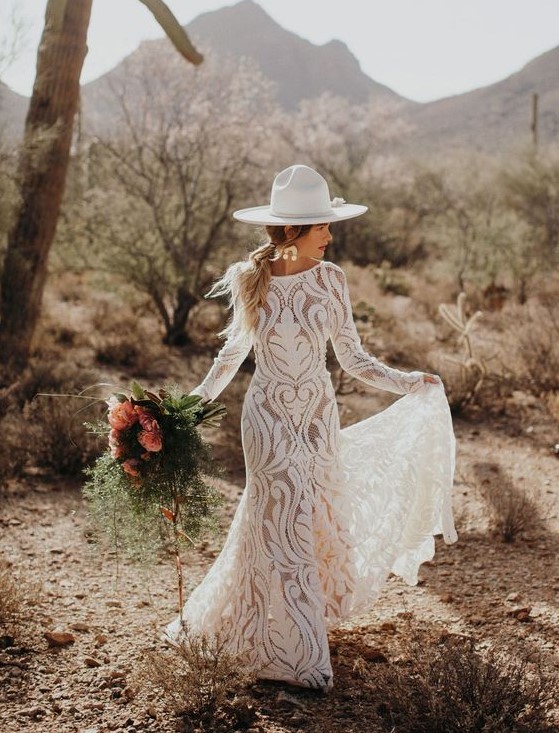 a fitting boho lace wedding gown with a high neckline and long sleeves, statement earrings and a white hat for a boho elopement