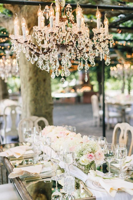 a glam wedding reception with neutral lush florals and a large glam crystal chandelier over the table is amazing