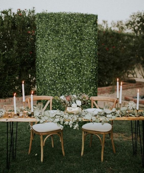 a greenery wall dotted with veyr small blooms is a stylish and bold wedding backdrop idea to rock