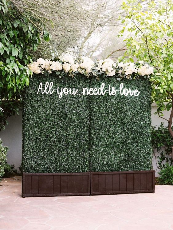 a greenery wall with a neon sign and some neutral blooms on top is a classic wedding ceremony backdrop to rock