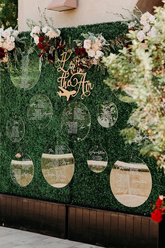 a greenery wall with an acrylic seating chart and some bold blooms on top is a very chic and bold idea for a wedding