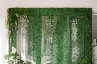 a greenery wall with ferns and foliage, candles and an acrylic seating chart is a very stylish idea for a modern wedding