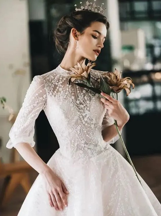 a jaw dropping lace applique and embellished wedding ballgown with a high neckline and short sleeves plus a crown