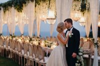 a jaw-dropping wedding reception roof covered with greenery and white blooms hanging down plus lots of crystal chandeliers over the space