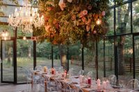 a lovely greenhouse wedding reception with lush florals and greenery hanging over the space and crystal chandeliers for more light and a glam touch