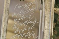 a mirror in a chic frame, with blooms and greenery and with white calligraphy is a stylish idea