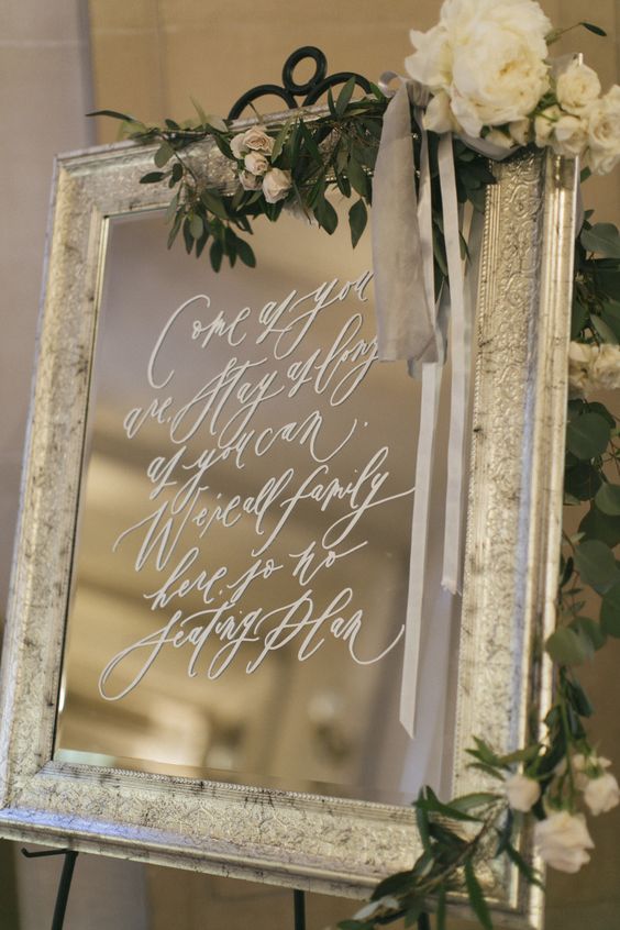 a mirror in a chic frame, with blooms and greenery and with white calligraphy is a stylish idea
